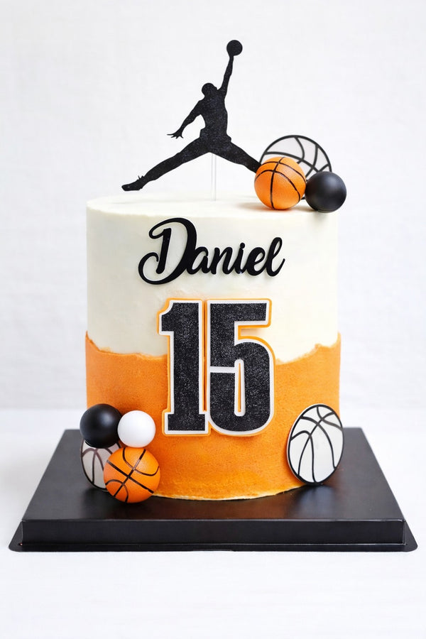 Basketbal taartdecoratie met zwart spelerssilhouet, naam Daniel en leeftijd 15 op een witte en oranje voorbeeldtaart